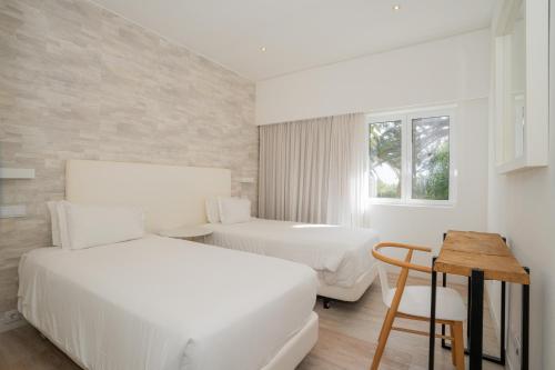 a white bedroom with two beds and a table at Dune Beach CoLiving in Porto Santo