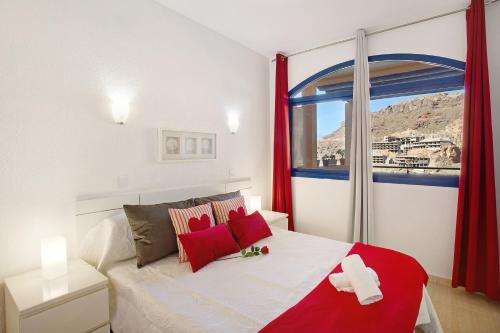 Schlafzimmer mit einem Bett mit roten Vorhängen und einem Fenster in der Unterkunft Paraiso Playa Taurito in Taurito