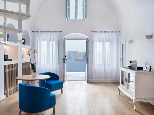 a living room with a table and blue chairs at Katikies Santorini - The Leading Hotels Of The World in Oia