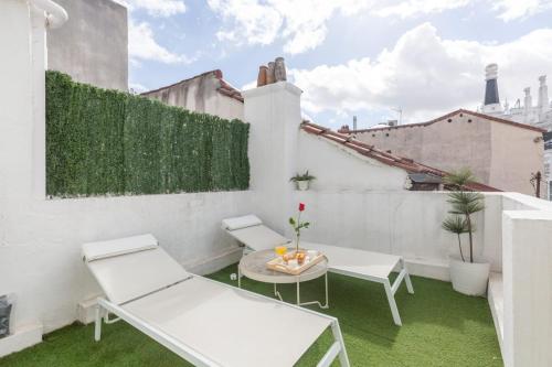 Un pequeño balcón con sillas blancas y una mesa. en Apartamento Ático Las letras, en Madrid