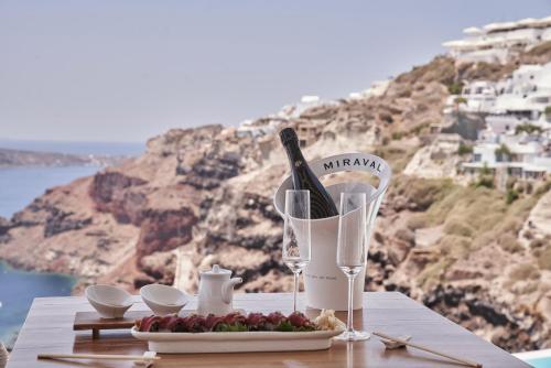 a table with a bottle of wine and a plate of food at Katikies Santorini - The Leading Hotels Of The World in Oia