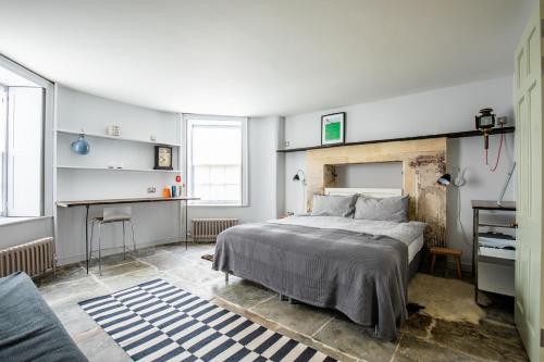 a bedroom with a bed and a desk and two windows at Walcot Apartment in Bath
