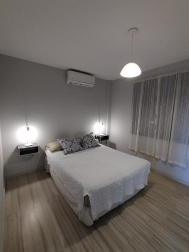 a white bedroom with a bed and two lamps at Departamento en San Nicolás de los Arroyos in San Nicolás de los Arroyos