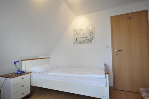 1 dormitorio con cama blanca y puerta de madera en Ferienhaus Wattje Am Yachthafen 102 E, en Harlesiel