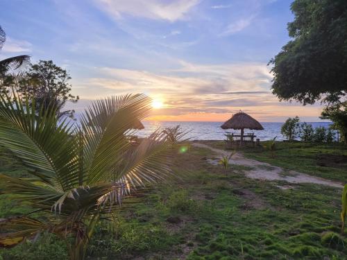 a sunset over the ocean with a grass umbrella at Casa Suite Palmar del viento FRENTE, FRENTE AL MAR by Amauna in Moñitos