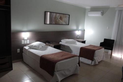 a hotel room with two beds and a chair at Class Hotel Passos Rio Grande Portal da Canastra in Passos