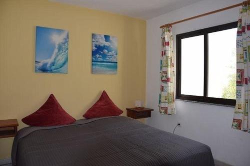 Un dormitorio con una cama con almohadas rojas y una ventana en Appartement in Betancuria mit Garten und gemeinsamem Pool, en Valle de Santa Inés
