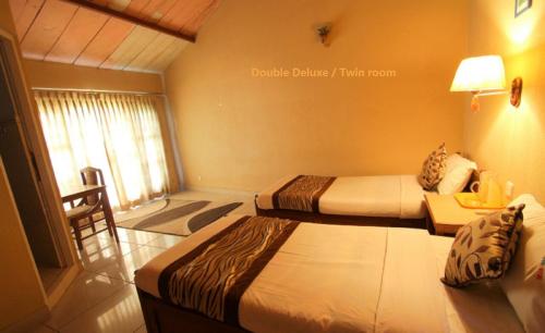 a bedroom with two beds and a table and a window at Baghmara Wildlife Resort in Sauraha
