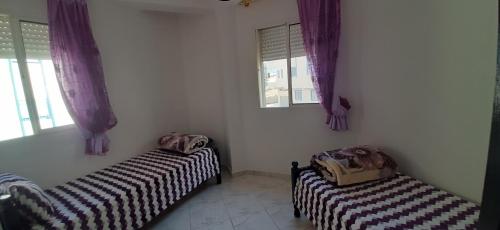 2 Betten in einem Zimmer mit lila Vorhängen in der Unterkunft APPARTEMENT AL HOCEIMA prés de PLAGE CALABONITA in Al Hoceïma