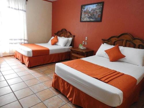 two beds in a hotel room with orange walls at Hotel Oaxaca Dorado in Oaxaca City