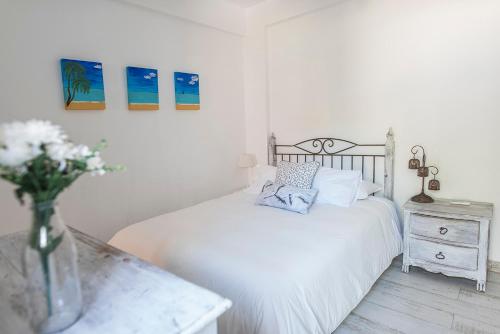 um quarto branco com uma cama e um vaso de flores em The Beach House em Vila Nova de Cacela