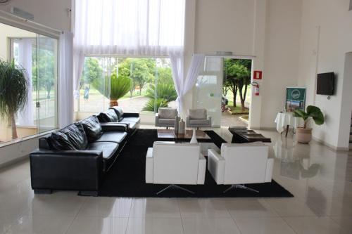 a living room with a black leather couch and white chairs at Class Hotel Passos Rio Grande Portal da Canastra in Passos