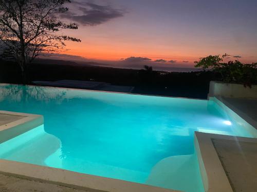 a blue swimming pool with a sunset in the background at Piscina vista al mar, Jacuzzi con agua caliente in Río San Juan