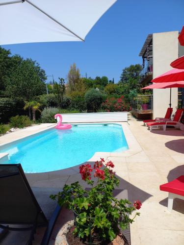 a swimming pool with a red umbrella and some flowers at Gîte Le Logis Vallat Bas in Fuveau