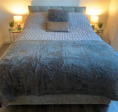 a large bed with a blue comforter and two lamps at BYRON SQUARE COTTAGE in Hucknall