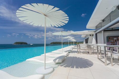 a pool with white chairs and umbrellas on a building at Kata Rocks - SHA Extra Plus in Kata Beach