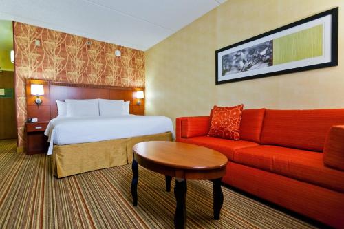 デスプレーンズにあるコー​​トヤード シカゴ オヘアのベッドと赤いソファが備わるホテルルームです。