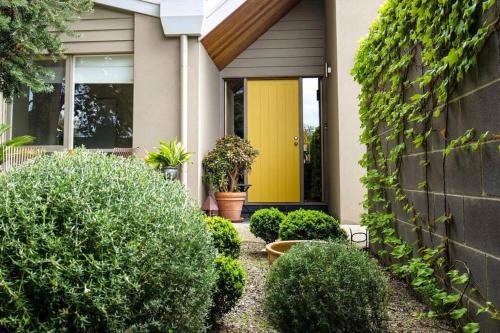 a house with a yellow door and some bushes at Yellow Door Villa in Barwon Heads