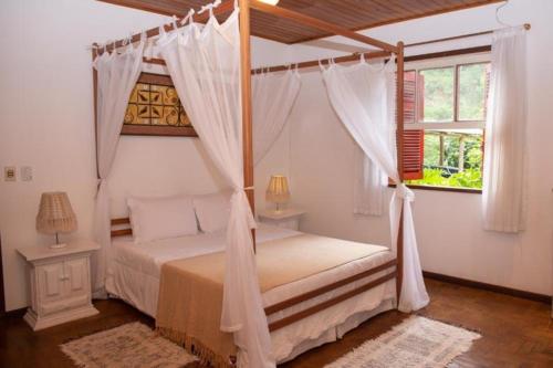 1 dormitorio con cama con dosel y ventana en Pousada Sitio e Poesia en Teresópolis