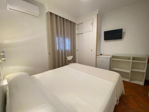 a bedroom with a white bed and a television at Hostal Los Mellizos in Conil de la Frontera