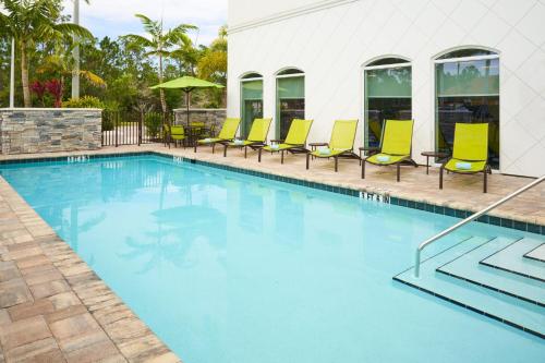 a swimming pool with yellow chairs and a building at SpringHill Suites by Marriott Fort Myers Estero in Estero