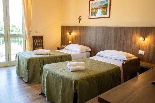 a hotel room with two beds with tables and a window at Hotel La Tavola Rotonda in Assisi