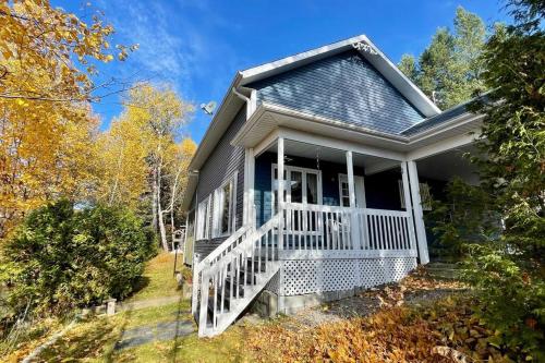 a small house with a porch and white railing at Le Chalet Bleu, aux pieds des Monts-Valin in Saint-David-de-Falardeau