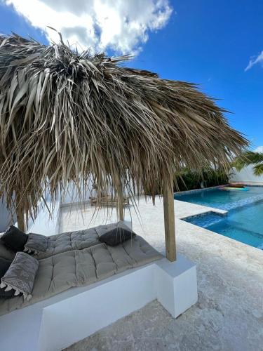 a bed under a straw umbrella next to a pool at Villa Hermosa in Bayahibe