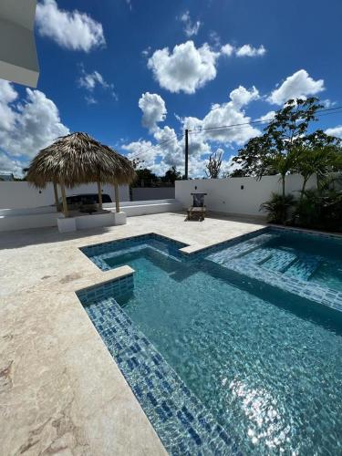 a swimming pool with a straw umbrella next to at Villa Hermosa in Bayahibe