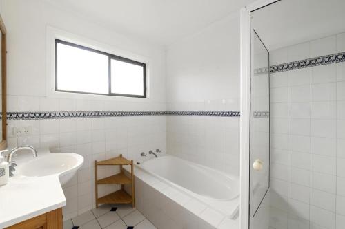 Baño blanco con bañera y lavamanos en Blue Oar Beach House Arrawarra Headland, en Arrawarra