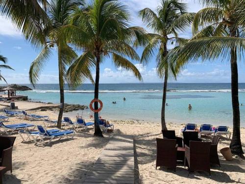 a beach with chairs and palm trees and the ocean at Studio 4 places chez Loïc in Saint-François