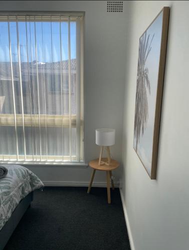 a bedroom with a bed and a window and a lamp at Eloura Gardens 100m to Beach in Cronulla