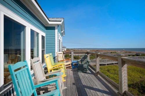 a row of chairs on a porch overlooking the ocean at Turtle Watch Too by Oak Island Accommodations in Caswell Beach