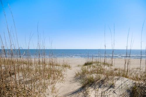 a beach with tall grass and the ocean at Turtle Watch Too by Oak Island Accommodations in Caswell Beach