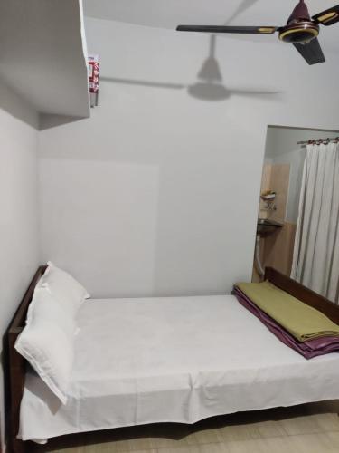 Newa Service Apartment في سيليغري: غرفة نوم بسرير مع شراشف بيضاء ومروحة