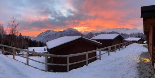 a winter sunset with snow covered buildings and mountains at Camping & Chalet Pian della Regina in Cevo
