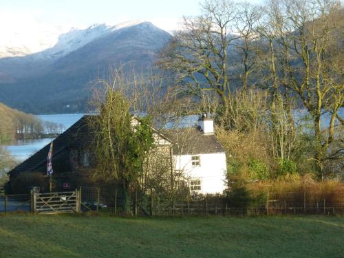 a house in a field with a lake and a mountain at Slack Cottage in High Wray