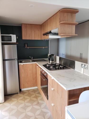 a kitchen with wooden cabinets and a stainless steel refrigerator at CAMPING SIBLU LA CARRABASSE MOBIL HOME OL21 in Vias