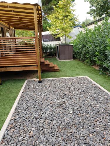 un jardin avec un banc et un patio en galets dans l'établissement CAMPING SIBLU LA CARRABASSE MOBIL HOME OL21, à Vias
