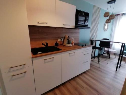 a kitchen with white cabinets and a sink and a table at Studio neuf - parking - 3 Epis proche Turckheim in Turckheim