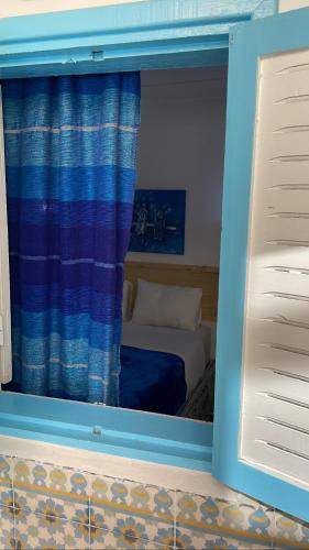 a room with a window with a bed and a curtain at Riad chez brahim in Essaouira