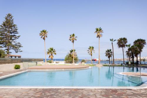 a swimming pool with palm trees and the ocean at Modern apartment with an addictive terrace view in Los Cristianos