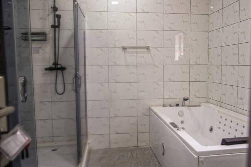 La salle de bains est pourvue de carrelage blanc, d'une douche et d'une baignoire. dans l'établissement TFP Lodge, à Ibadan