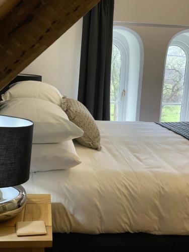 a bed with white sheets and pillows and two windows at Caemorgan Mansion in Cardigan