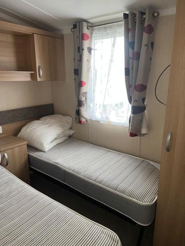 a small room with two beds and a window at 3 Bed Platinum Caravan PRESTHAVEN SANDS in Prestatyn