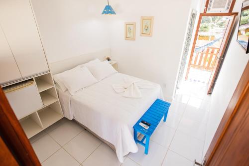 a small bedroom with a white bed and a blue chair at Pousada dos Corais in Itaúnas