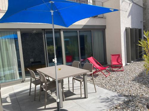 a table and chairs with a blue umbrella on a patio at MarAvilia Apartment - vicino a Splash & SPA Tamaro in Monte Ceneri