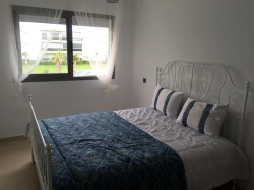 a bedroom with a bed with a blue and white bedspread and a window at Grand Apartement a Blanca Beach Sidi Rehal in Sidi Rahal