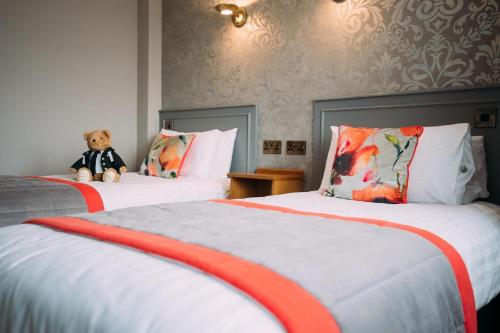 a teddy bear sitting on two beds in a hotel room at The Valley Hotel & Carriage Gardens in Fivemiletown