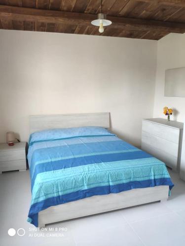 a white bedroom with a blue bed and two dressers at Casa vacanze La Meridiana in Donnalucata